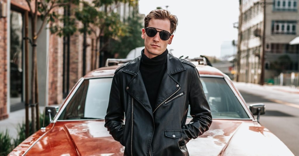 a fashionably dressed white man with sunglasses posing in front of a car. Make Money With Your Car.